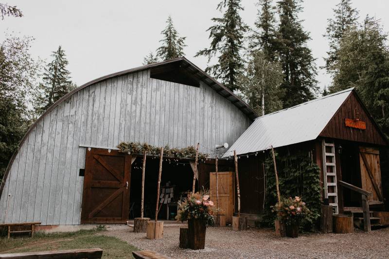 Barn with fairy light wedding arch in the forest with blush floral arrangements 