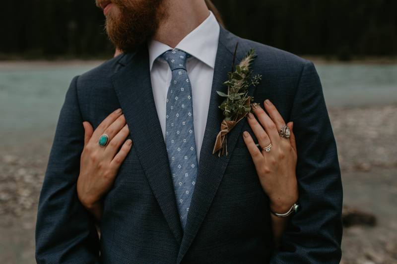 Groom wearing suit with dark green boutonniere and brown blue tie 