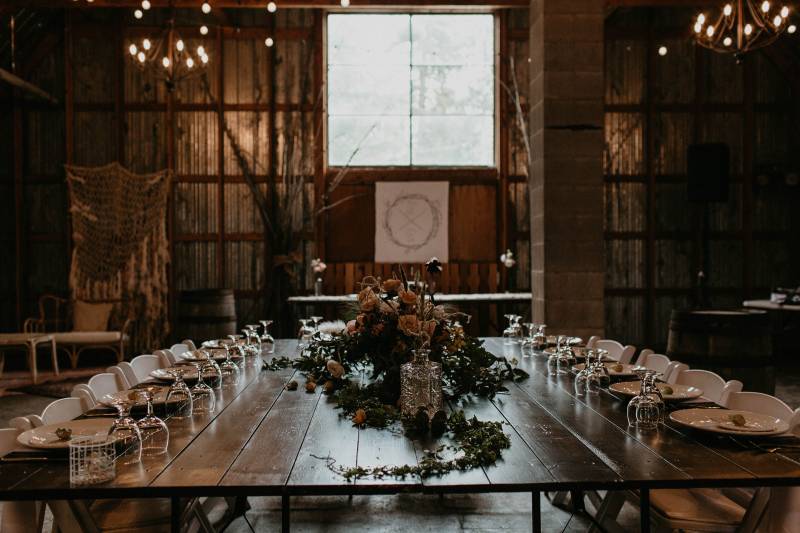 Barn wedding reception head table with green floral table runner and white table scape 