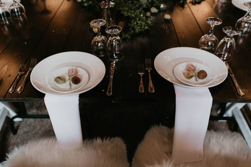 Wedding reception place setting with white fur seat covers and white place setting on dark wood table