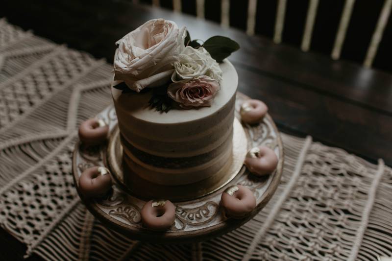 Powder green wedding cake with blush accents and floral decoration on macramé table lay  