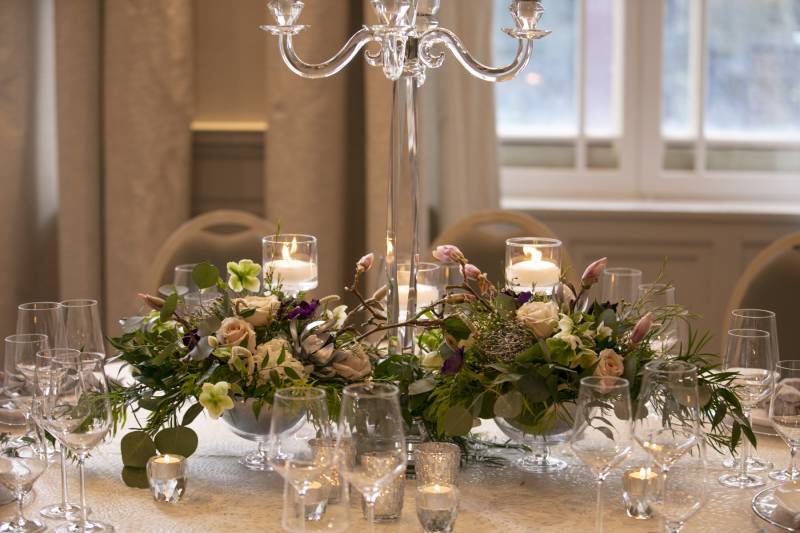 Glass centerpiece with green and blush floral arrangement on white table 