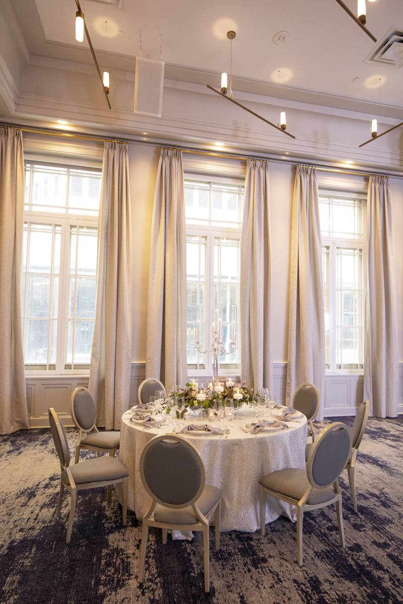 Large empty white room with long beige curtains with single table and seating around it 
