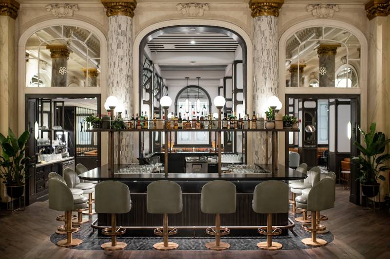 Luxurious bar in the middle of room with large marble pillars and bronze seating 