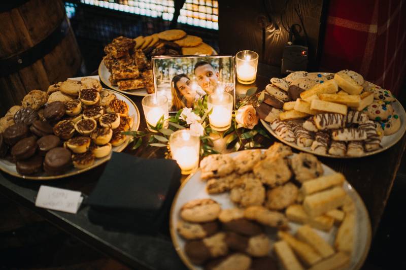 Various baked treats displayed on plates surrounding candle lit photo of bride and groom 