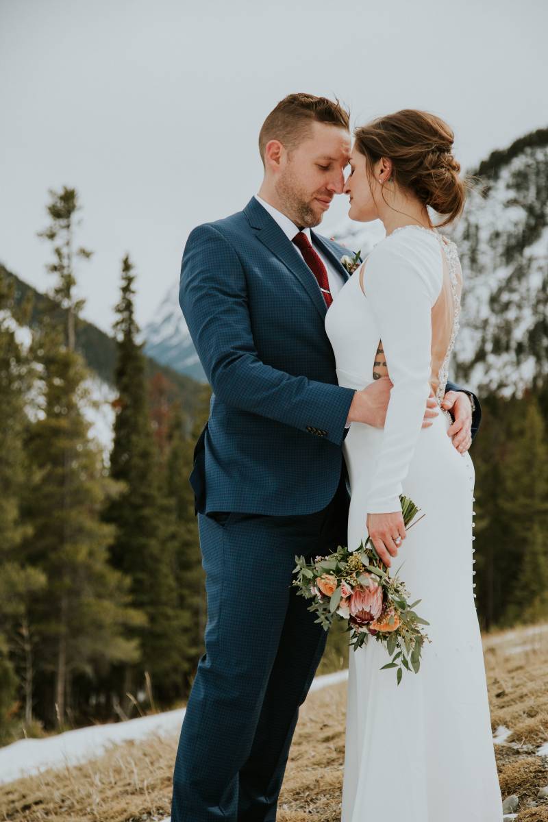 Bride and groom embrace on forested mountain slope
