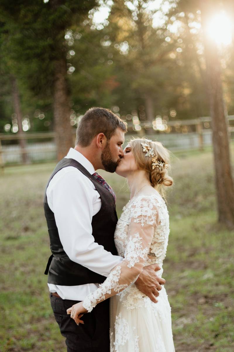Bride and groom kiss in front of forested backdrop 