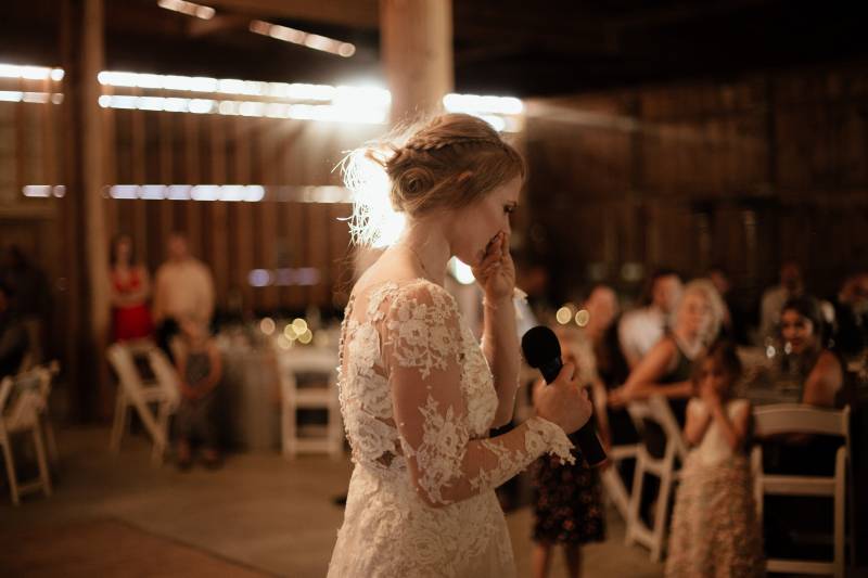 Bride in sleeved white lace bodice dress speaking into microphone 