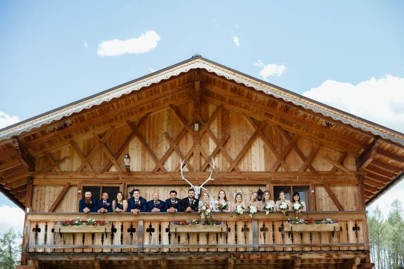 bride and groom and Bridesmaids and groomsmen leaning on wood cabin deck railing 