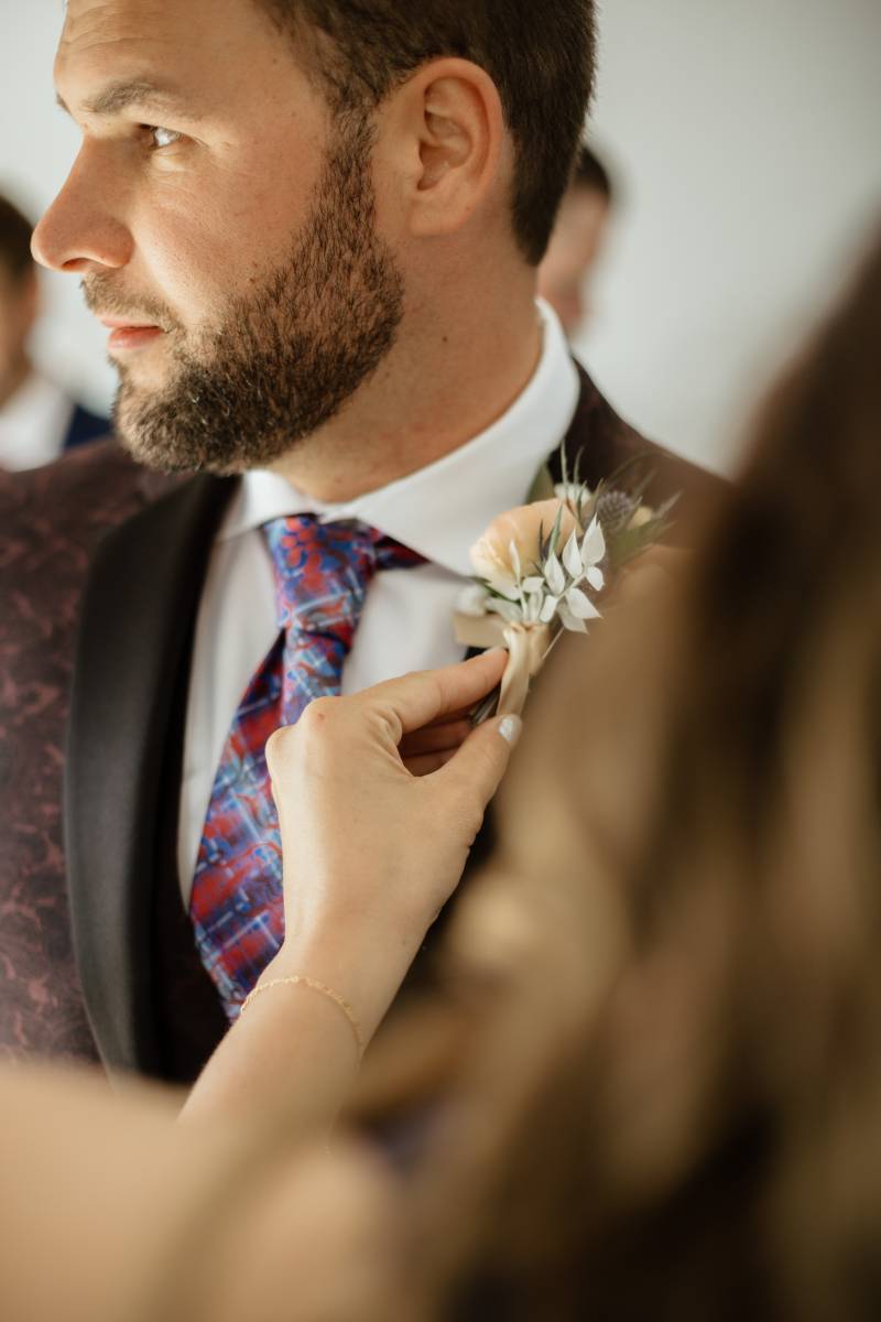 Groom being fitted with boutonniere looking to the side  