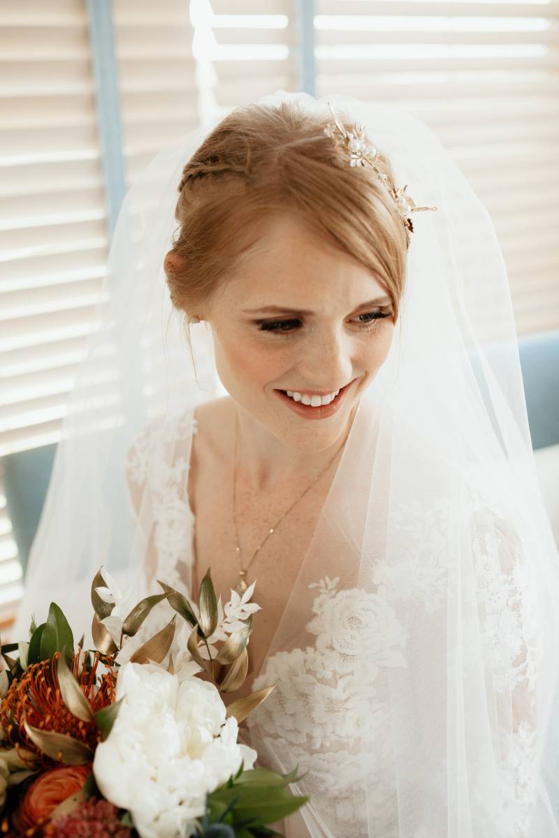 Bride with white veil holding bouquet with white pink and orange flowers  
