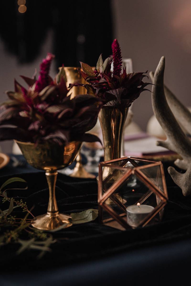 Gold goblets with burgundy floral arrangements on black table beside horns 