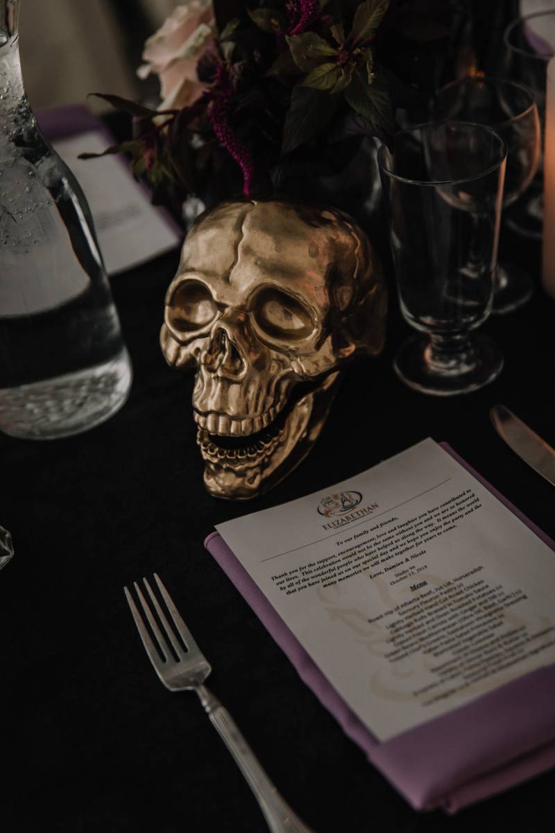 Golden skull centerpiece on black table setting with burgundy centerpiece 