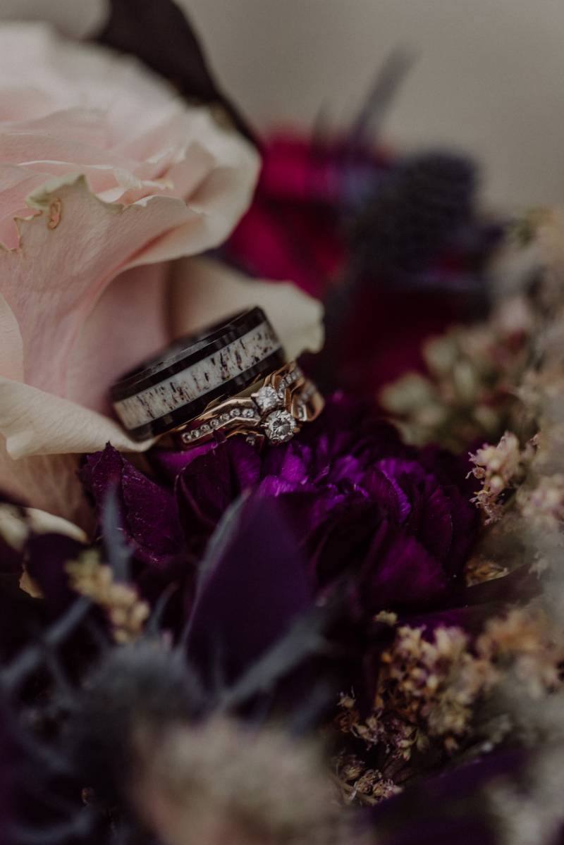 Bride and groom rings stacked on top of dark purple and pink flowers