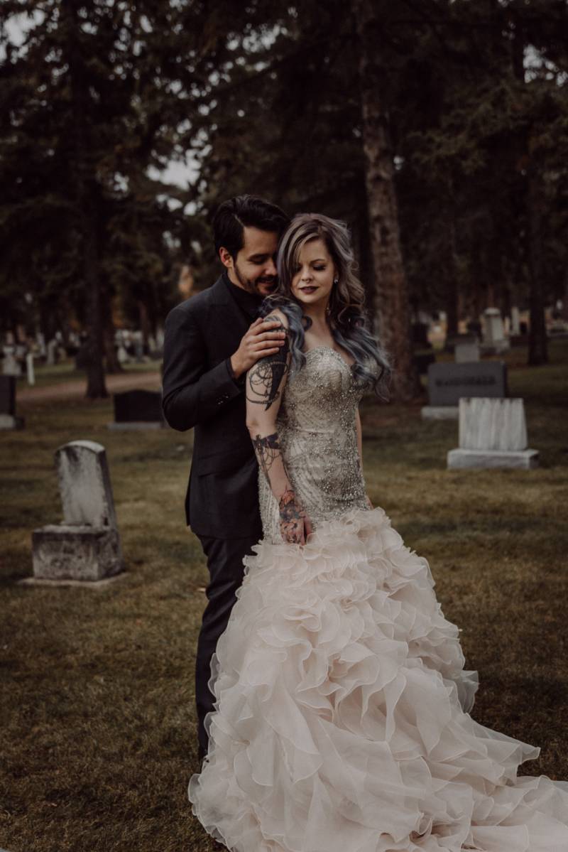 Groom touches shoulder of bride wearing large white dress in cemetery 