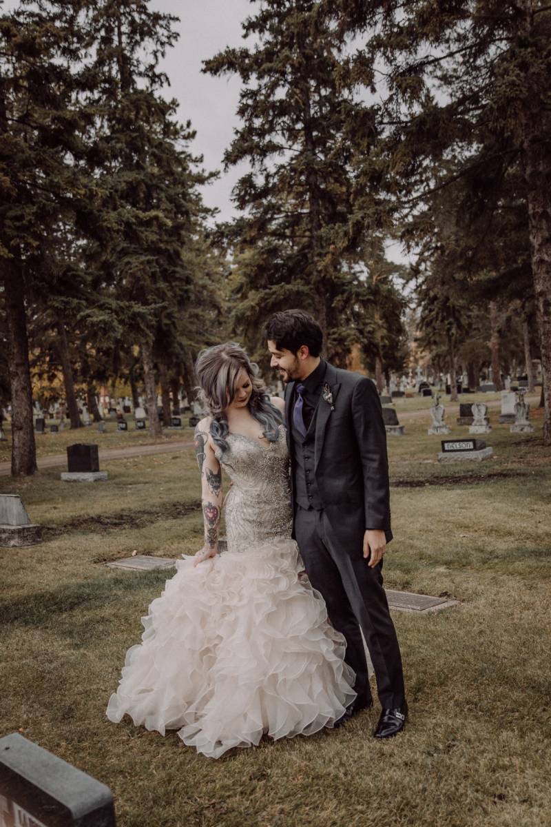 Bride in large white dress and groom stand together in cemetery 