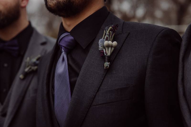 Beige boutonniere on chest of groom in black suit and purple tie 