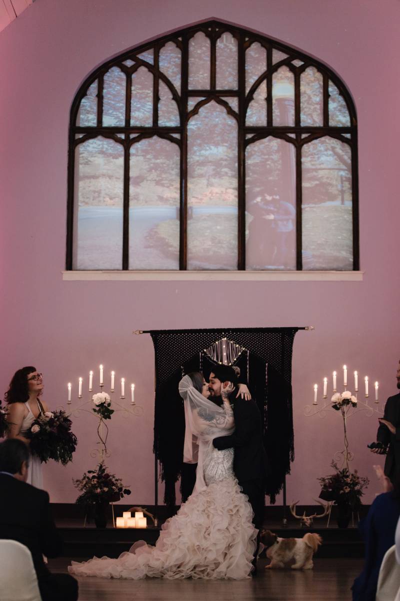 Bride and groom kiss in front of black macramé wedding arch and candelabras 