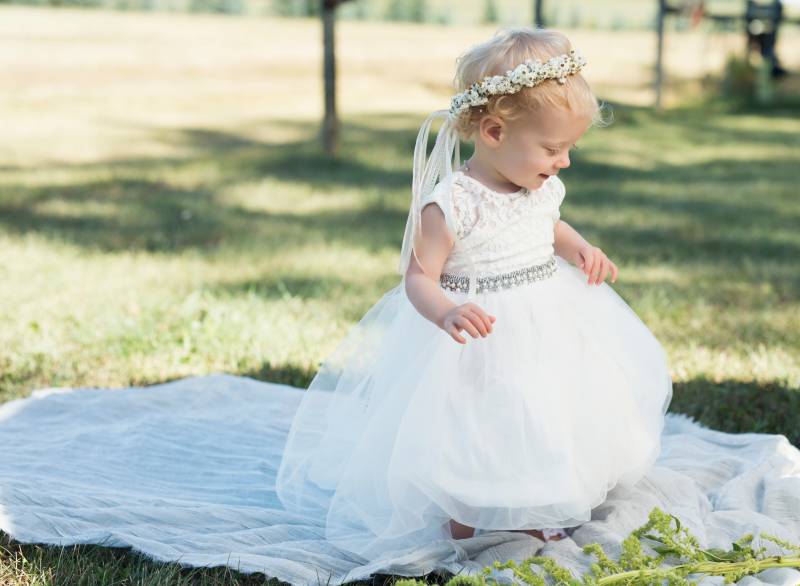 Flower girl with white flower crown walks on white fabric in grassy field 