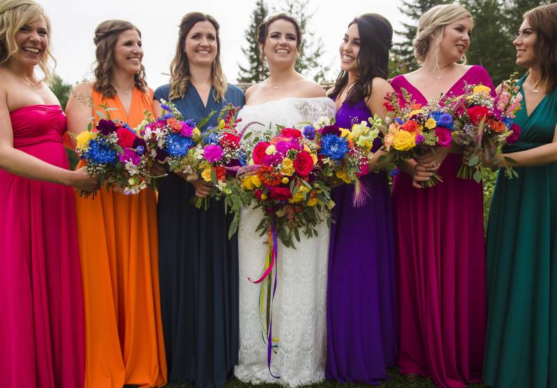 Bride and bridesmaids stand together holding bouquets in line smiling