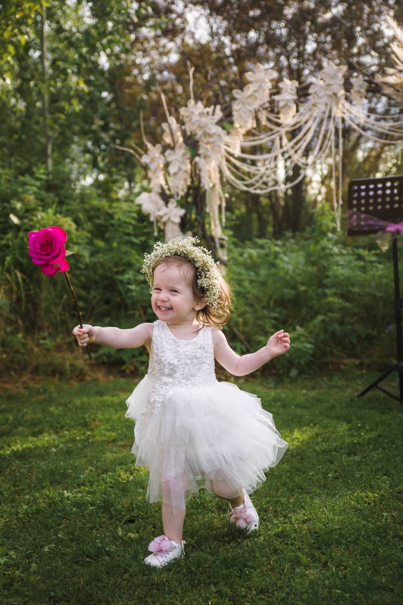 Child in large white dress and flower crown holding violet rose 