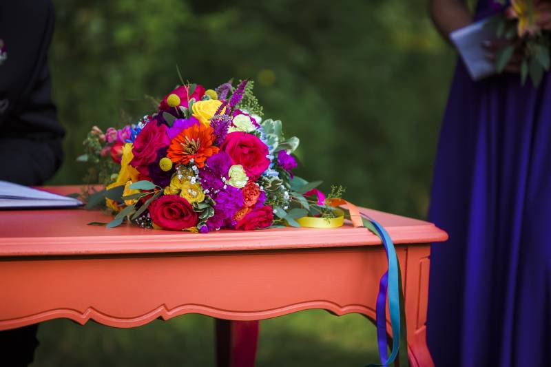 Multicolored floral bouquet with blue ribbons sitting on orange table  