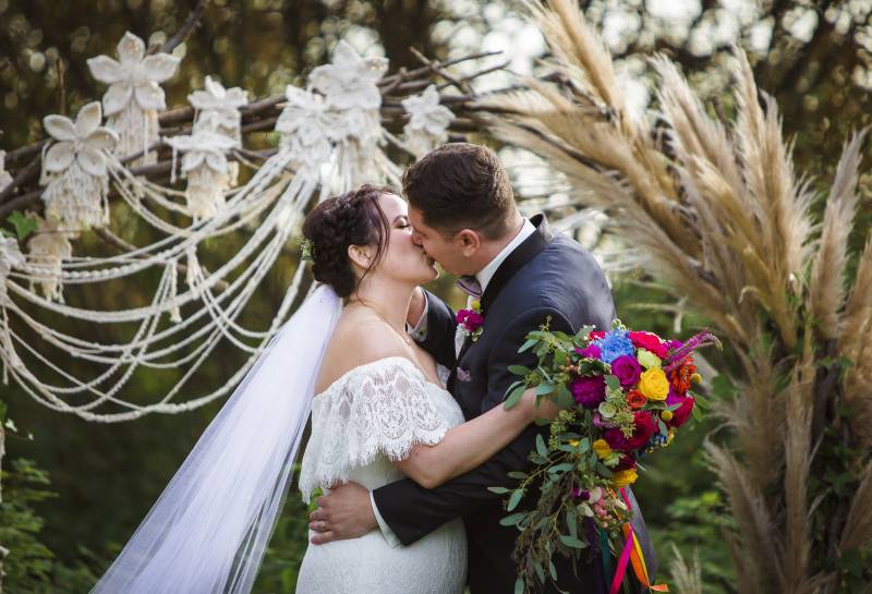 Bride and groom kiss in front of macramé wedding arch 