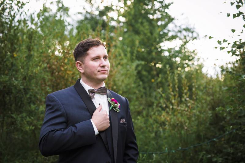 Man holding hand on chest with violet boutonniere looks off in distance 
