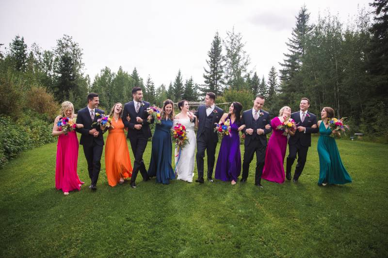 Bridesmaids and groomsmen stand arms linked in grassy field 