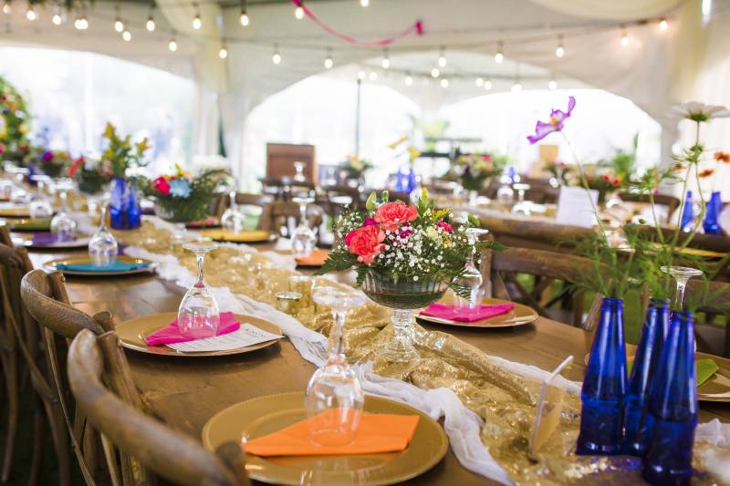 Multicolored table setting on wooden table with gold table runner and blue bottles with flowers