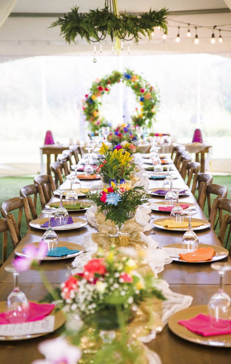 Wedding reception table scape with multicolored place settings and large floral centerpieces 