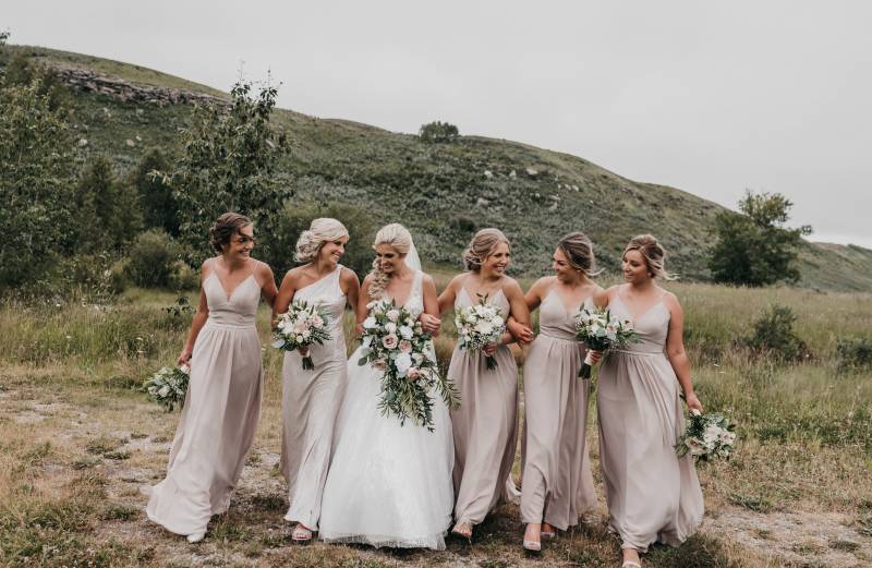Bride walks together in between bridesmaids holding white and blush bouquets 