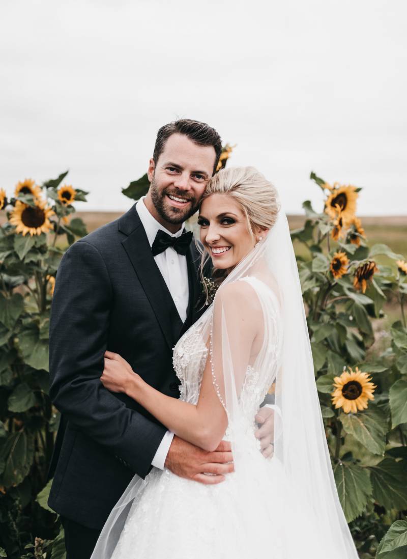 Bride and groom embrace smiling in front of sunflower patch