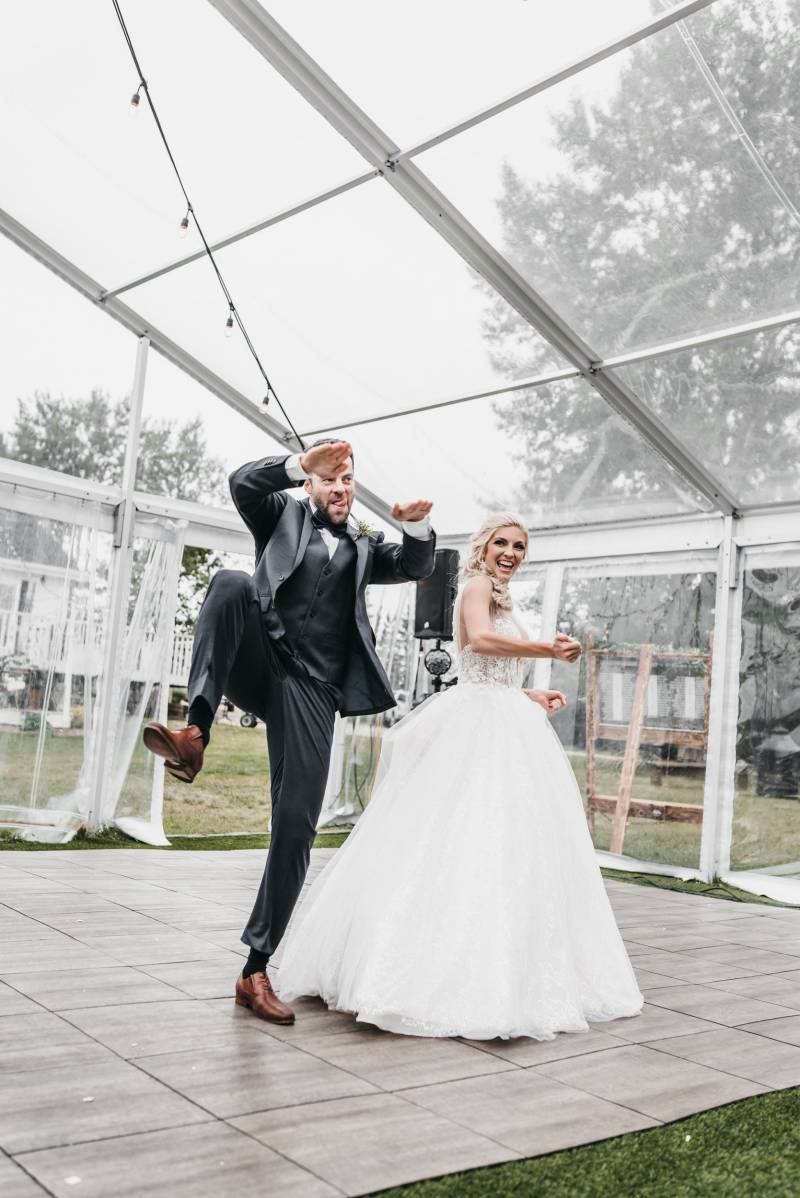 Groom stands on one leg hands up tongue out while bride smiles off to side  