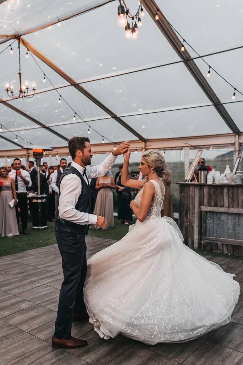 Groom spins bride while white dress spins out while guests watch behind 