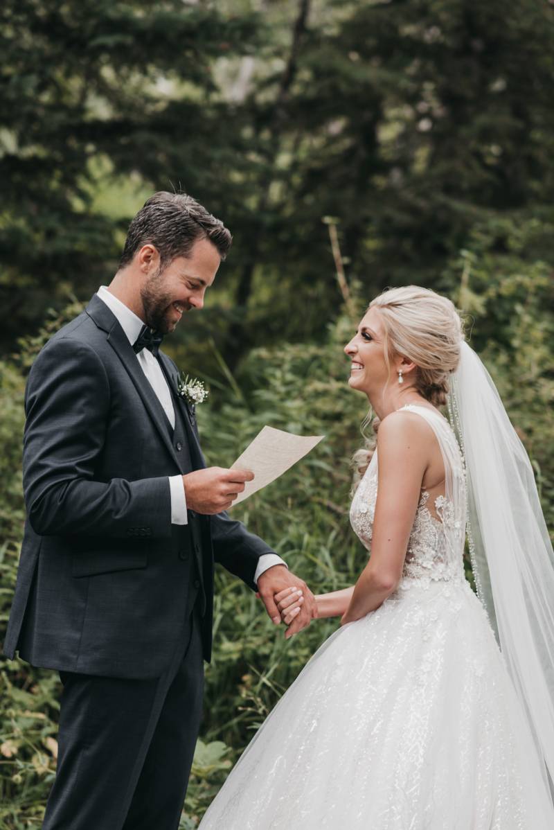 Bride holds grooms hand and he reads small white note smiling 