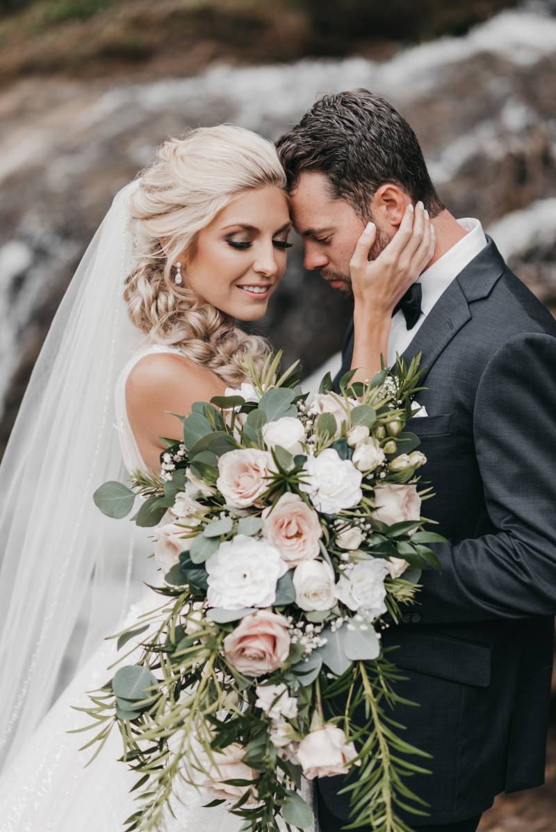 Bride touches grooms face while blush and white bouquet is held in front 