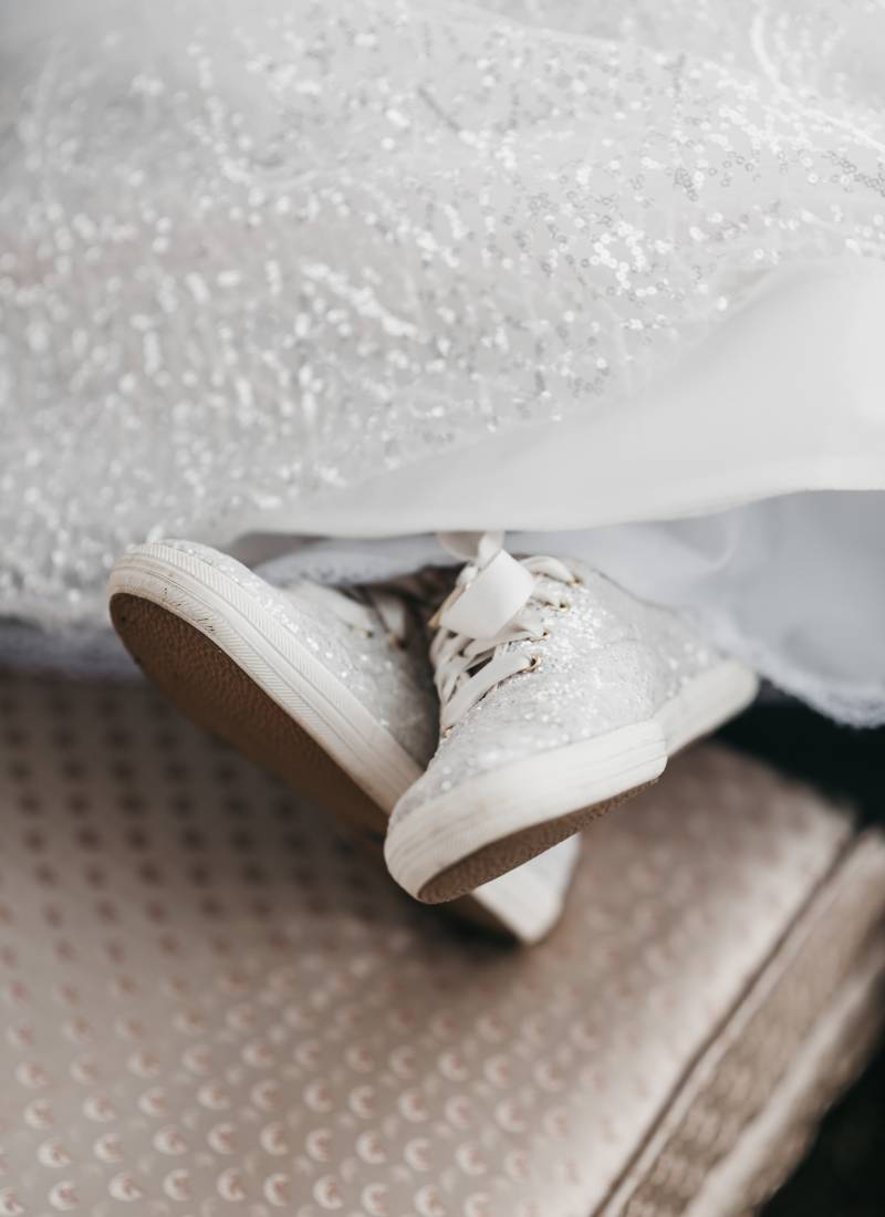 Sparkling white sneakers crossed under white dress 