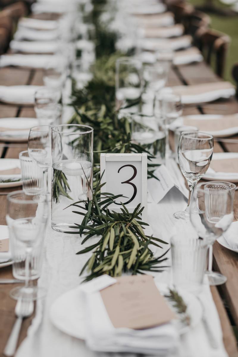 Place setting and table number on long wooden table with green table runner 