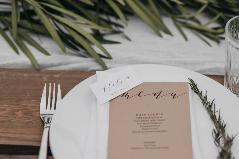 Place setting with brown menu and sprig of green on white napkin
