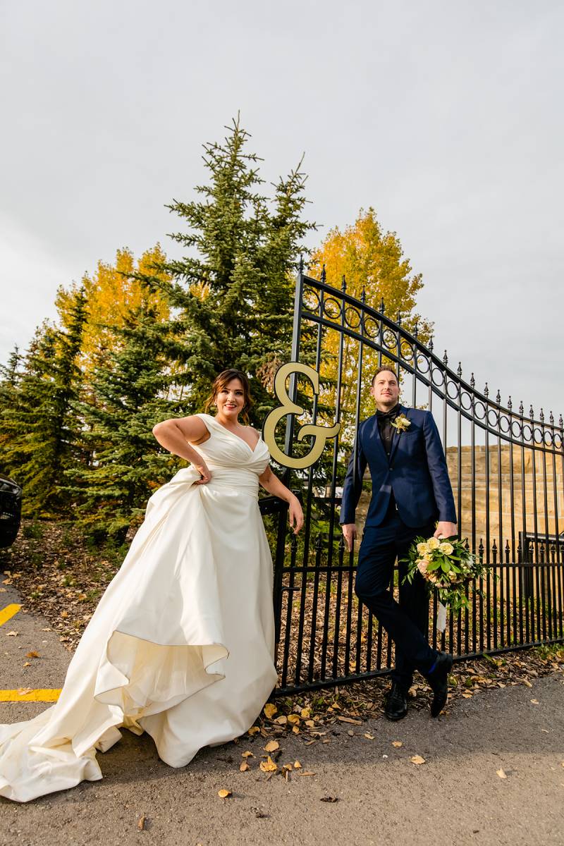 Bride and groom stand against black metal fence with gold letter