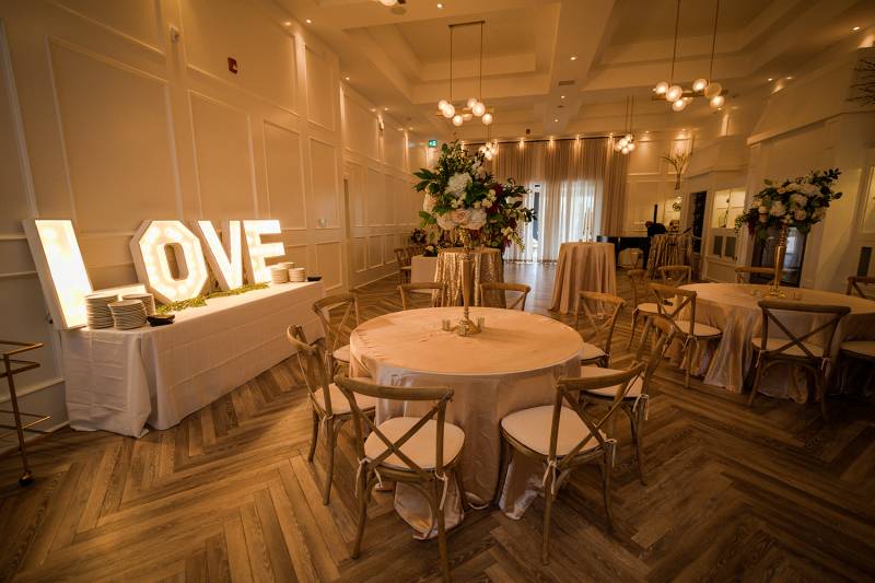 Large white dining room with wooden chairs around white tables and large illuminated love sign 