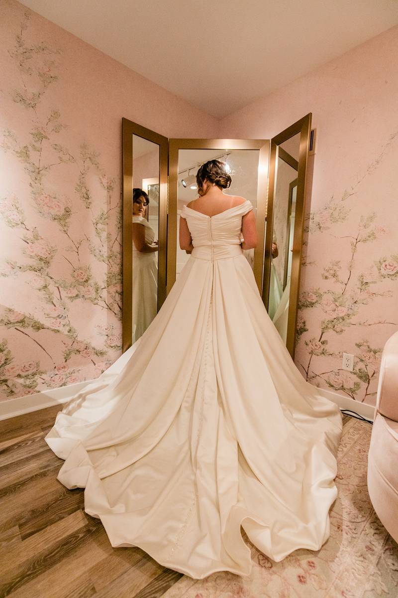 Bride stands towards mirror in large white dress 