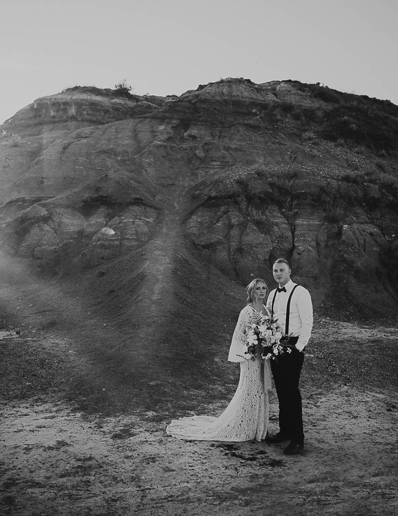 Man and woman stand in front of large dirt hill 
