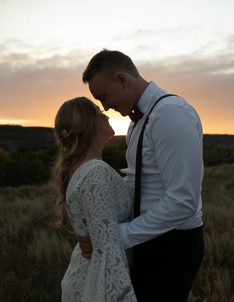 Man embraces woman in grassy field at sunset 