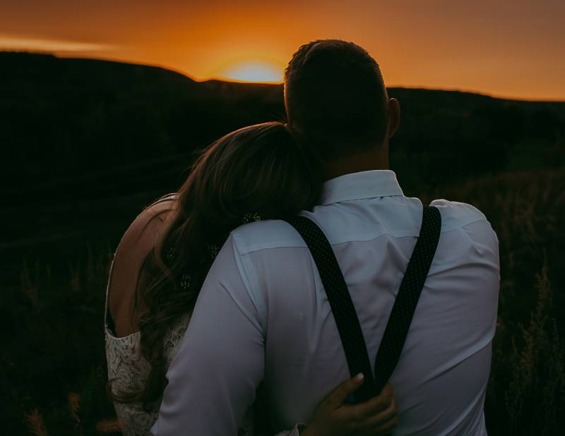 Woman leans on mans shoulder sitting looing at sunset 