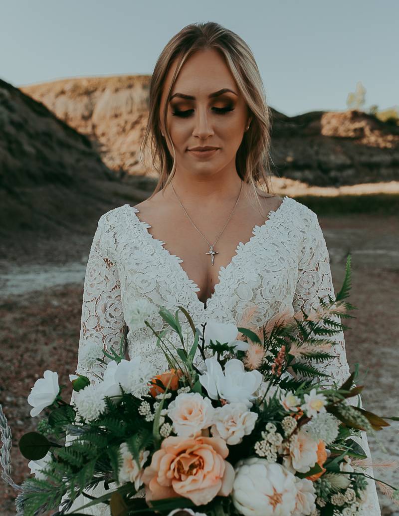 Bride looks down in white lace dress at peach and white bouquet 