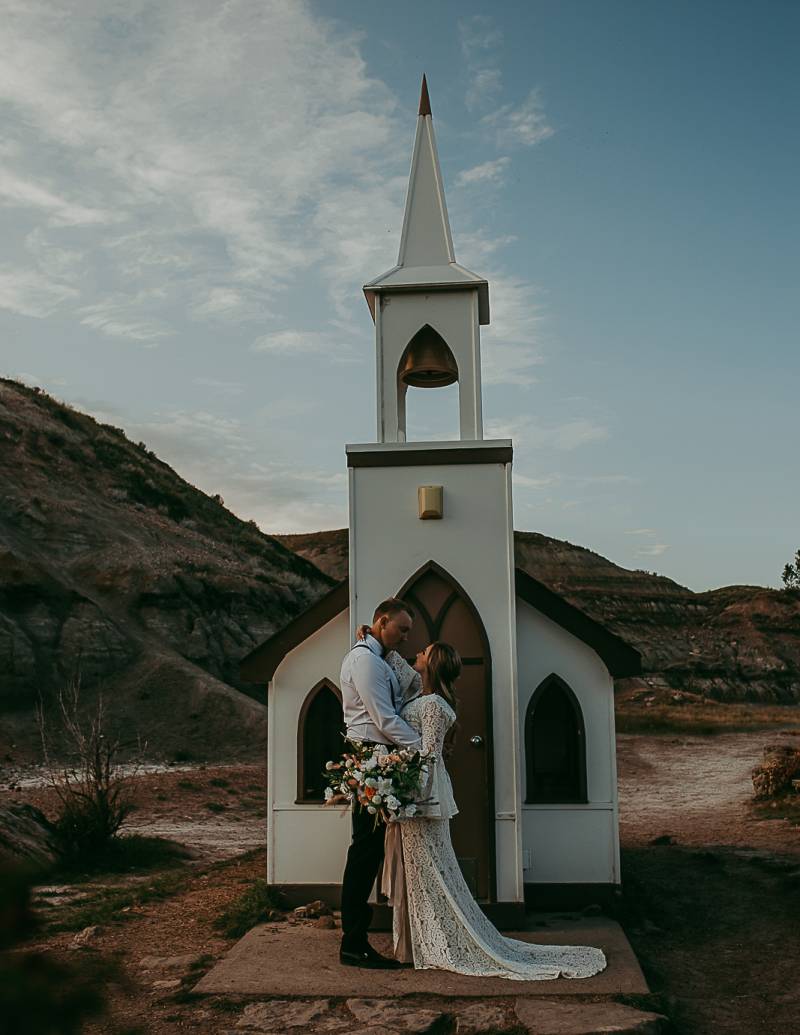 Man and woman stand embraced in front of miniature white church