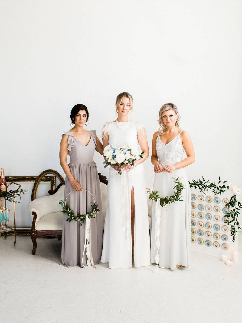 Three woman standing together holding bouquets and wreaths beside doughnut wall
