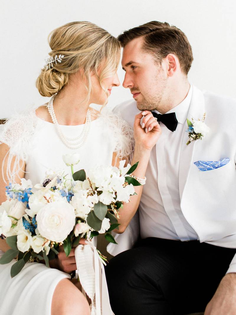 Man and woman gaze into each others eyes touching chin holding white bouquet